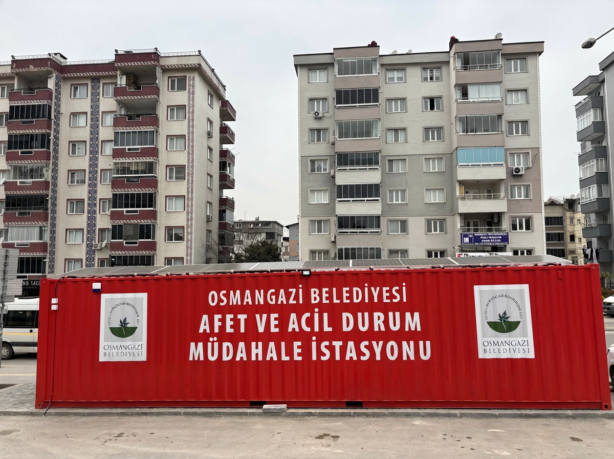 Bursa Korupark bölgesi civarında apartmanların arasına konumlandırılmış, çatısında off-grid güneş paneli sistemi bulunan kırmızı Osmangazi Belediyesi afet ve acil durum müdahale istasyonu.