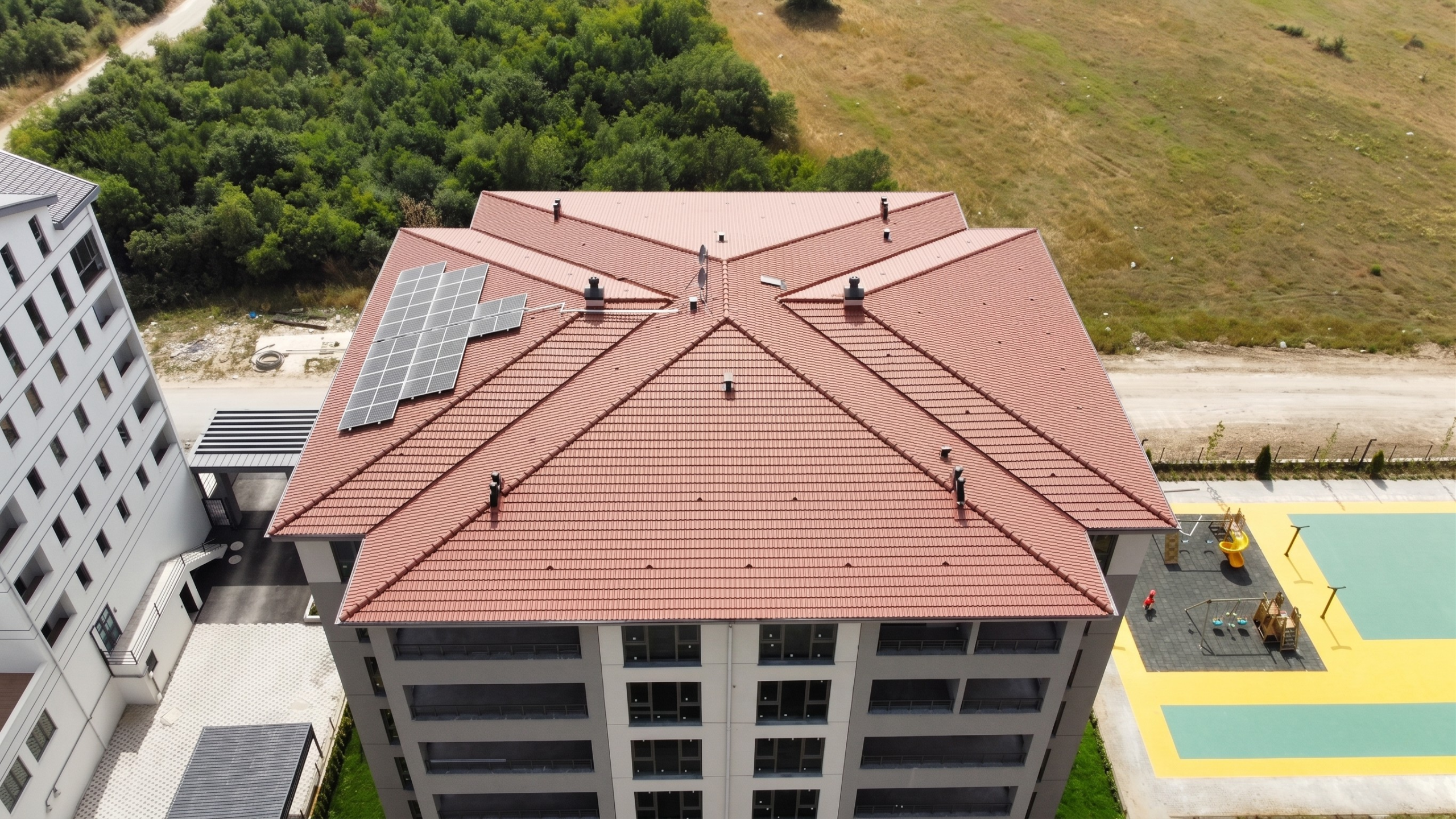 Bursa'da çocuk parkı bulunan bir apartman sitesinin çok cepheli kırma kiremit çatısında, güneye bakan alana özel tasarlanmış ortak alan güneş enerjisi panelleri.